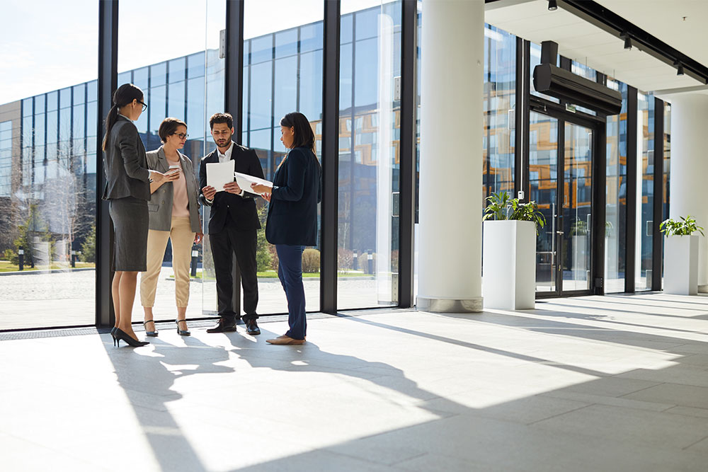 Group of creative interracial business people in formal outfits standing near panoramic window and analyzing paper data together