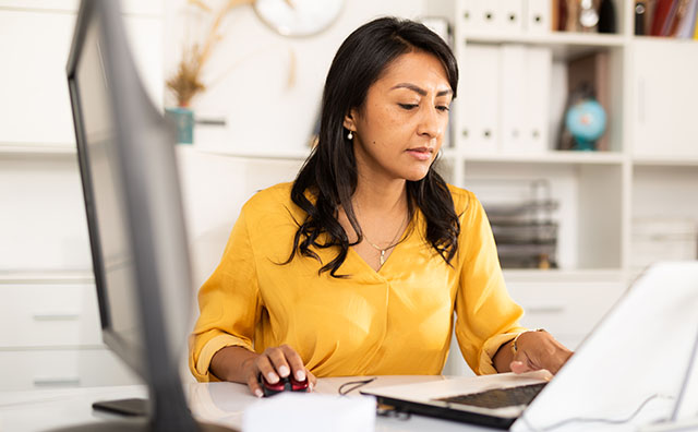 Latin American businesswoman sitting in office at workplace and working at laptop
